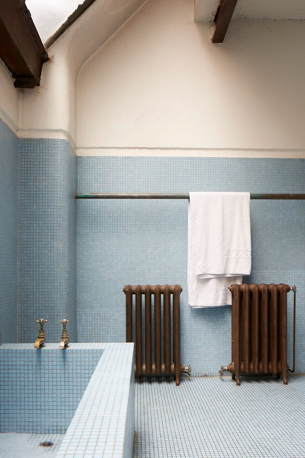 The blue tiled bathroom is separated from the main bedroom by a wooden partition behind the bed creating flow between...