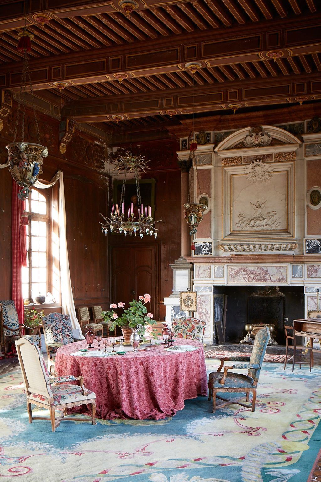 A large marble fireplace faces a low table in the Château de Sully dining room. The dusty pink tablecloth matches the...