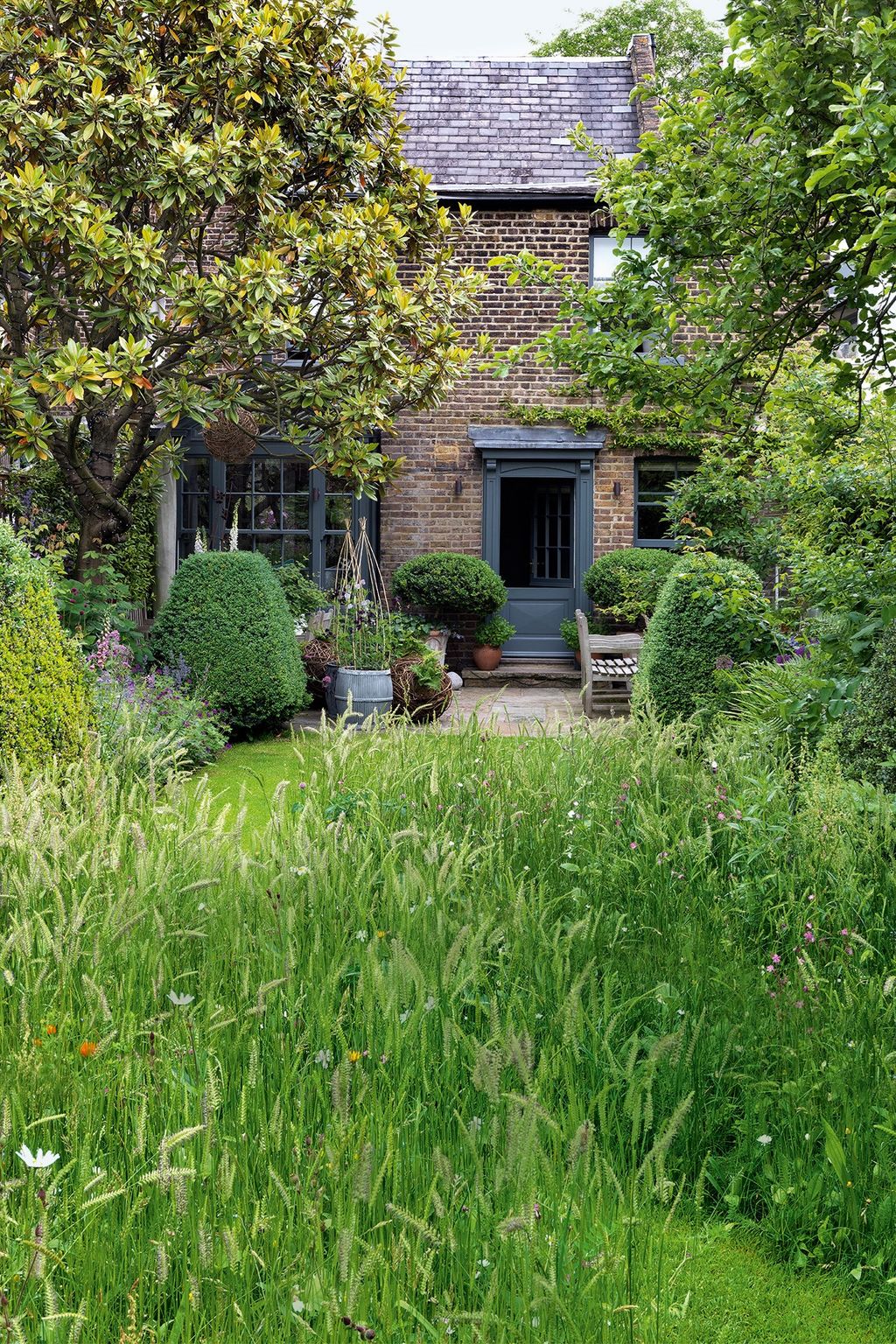 Image may contain Outdoors Garden Arbour Grass Plant Cottage Housing House Building Vase Pottery and Potted Plant