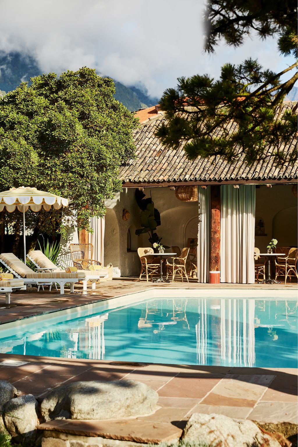 The Slim Aaronsinfluenced pool area at Villa Arnica in Lana features retroinspired parasols and sun loungers on a...