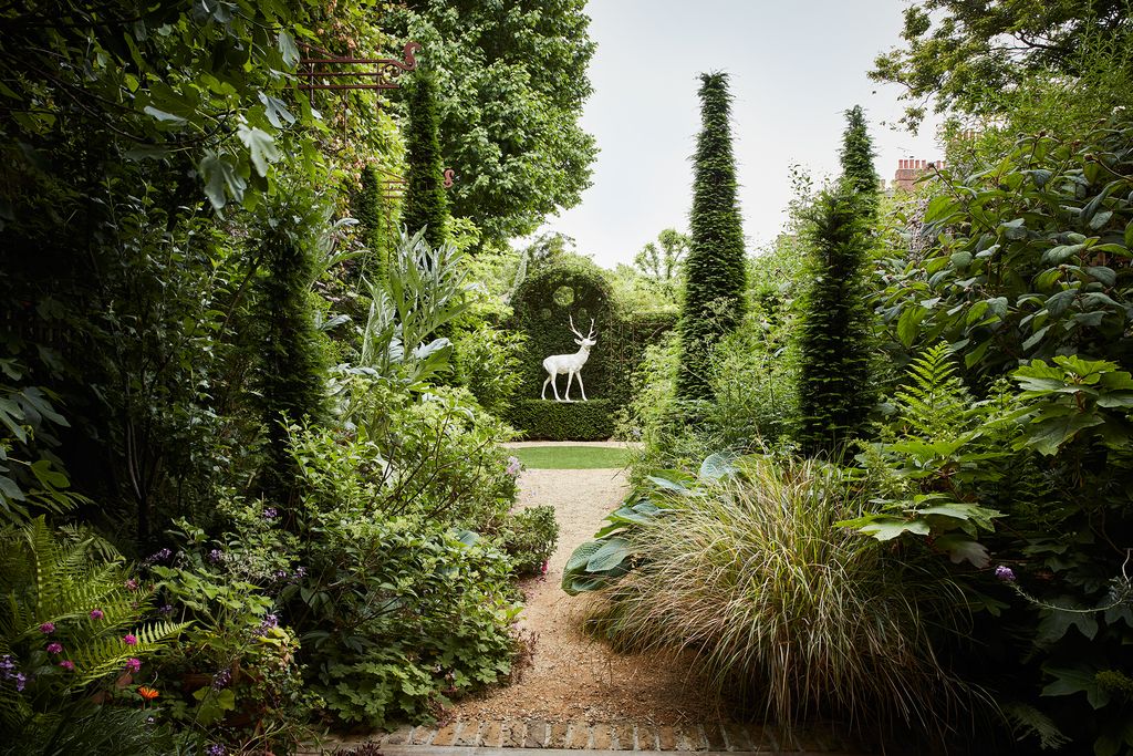 Plantings of pheasant grass cardoons and hostas are punctuated by yew spires which frame the view towards an antique...