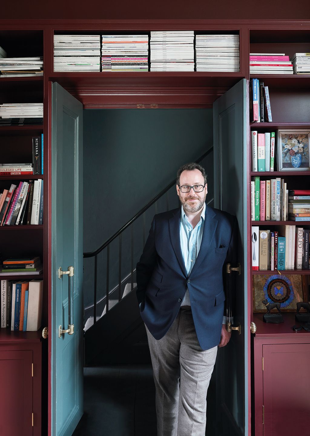 Image may contain Furniture Shelf Bookcase Human Person Suit Coat Clothing Overcoat Apparel Room and Indoors