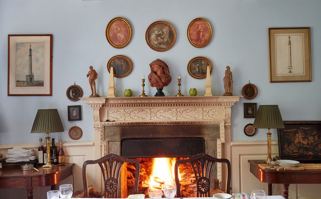 In perfect Georgian style the pale blue dining room has a cluster of prints and medallions hung above and around the...