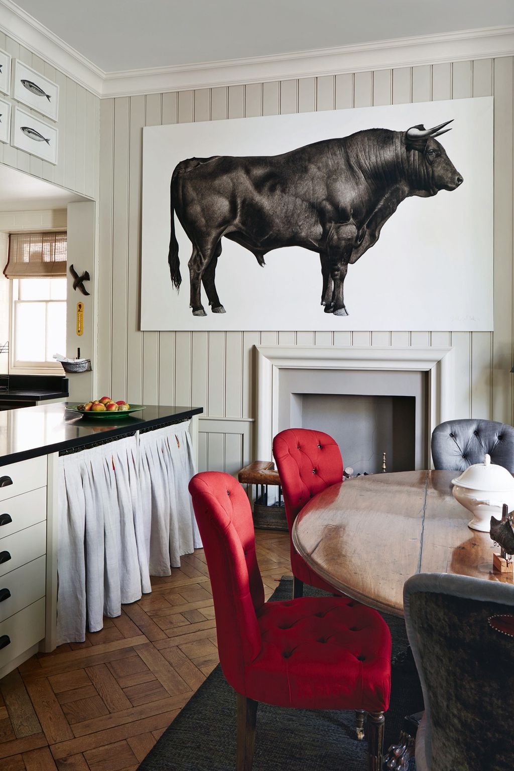 The red accents of the drawing room continue into the adjacent kitchen in the form of Howe chairs around the oval dining...