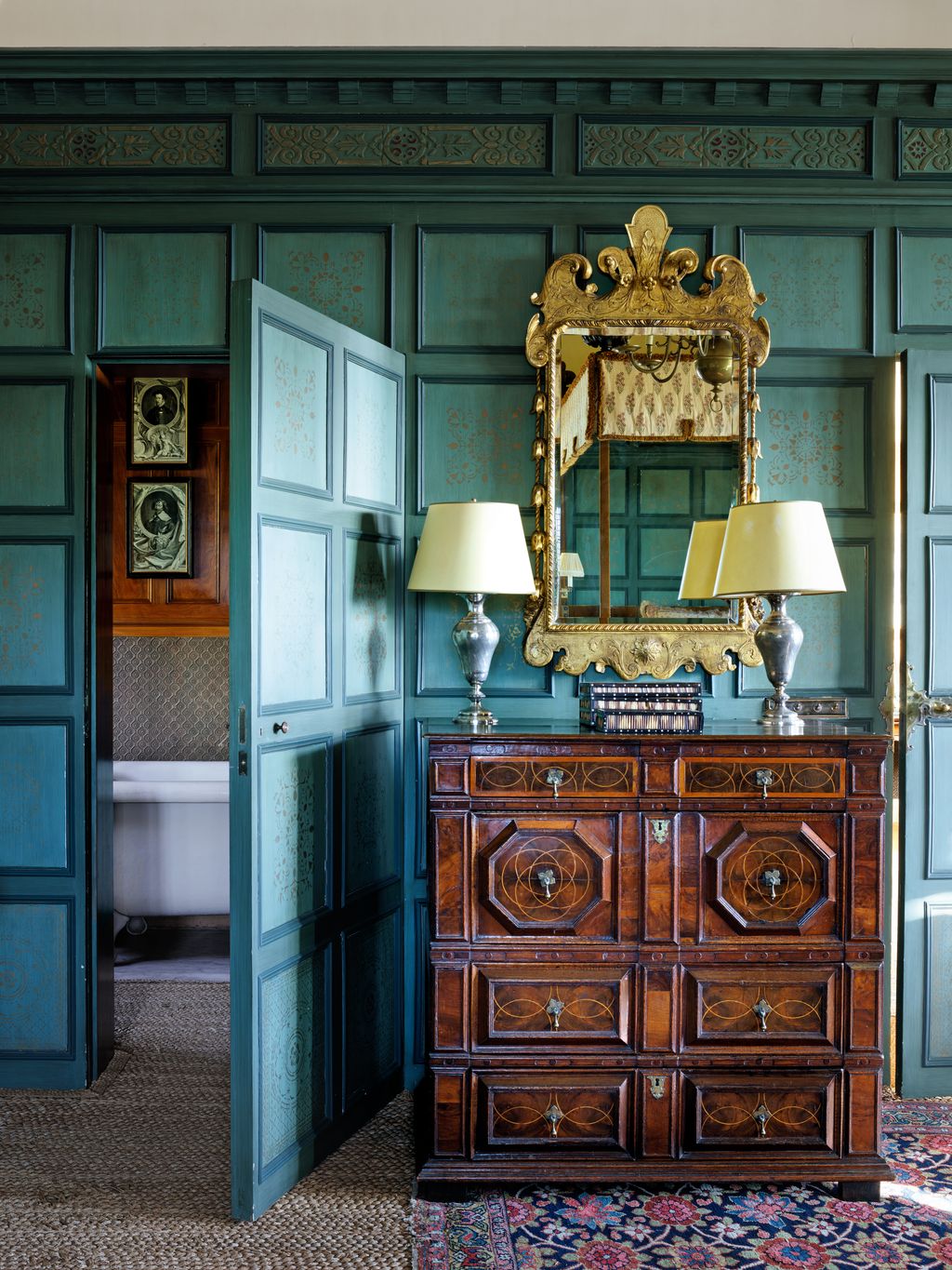 Subtly stencilled panels are the backdrop for a Queen Anne giltframed mirror above a chest of drawers bearing a pair of...