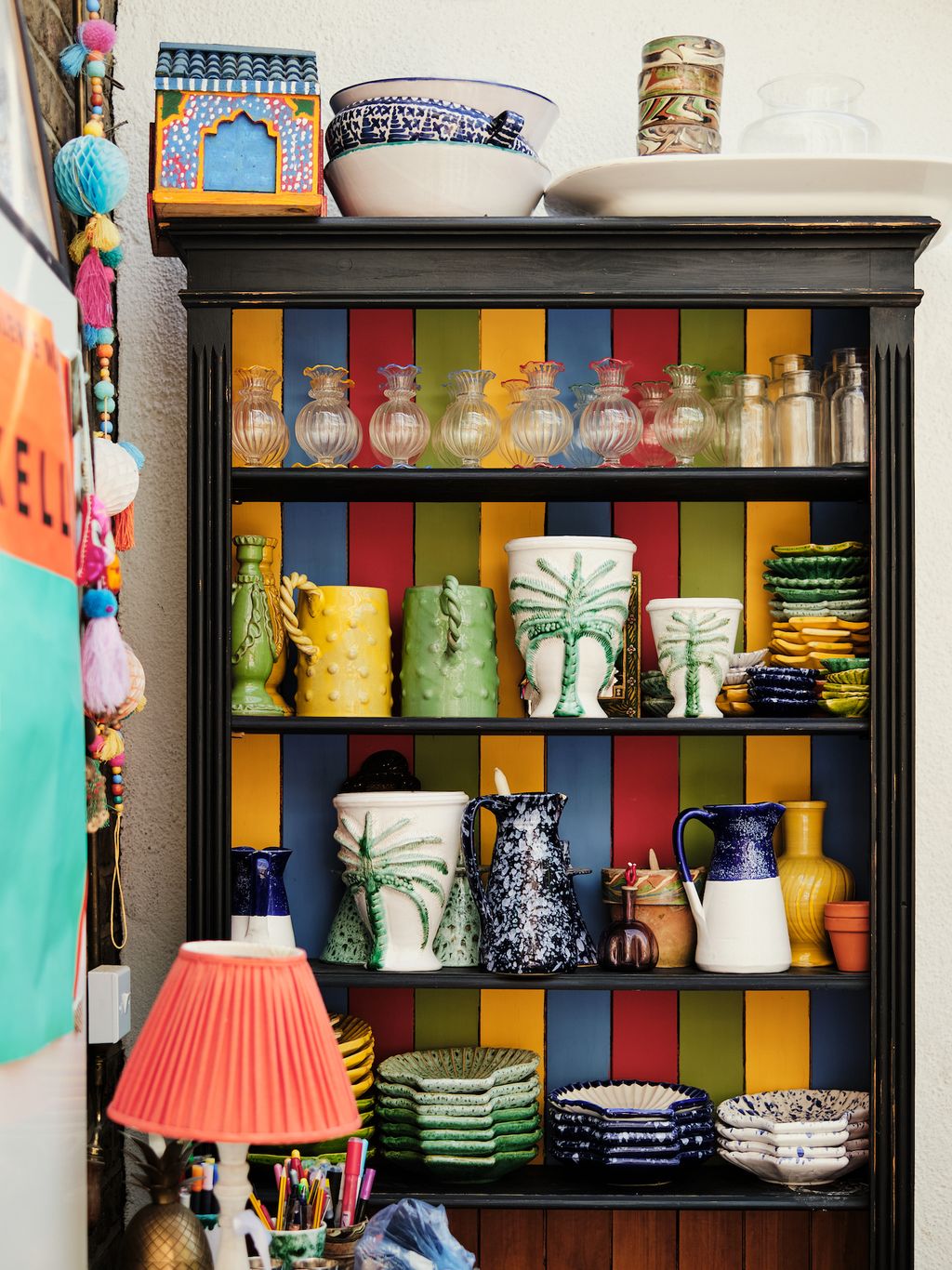 A bookcase was sourced from Kempton Market has been painted with Farrow and Ball sample pots. On the top shelf are glass...