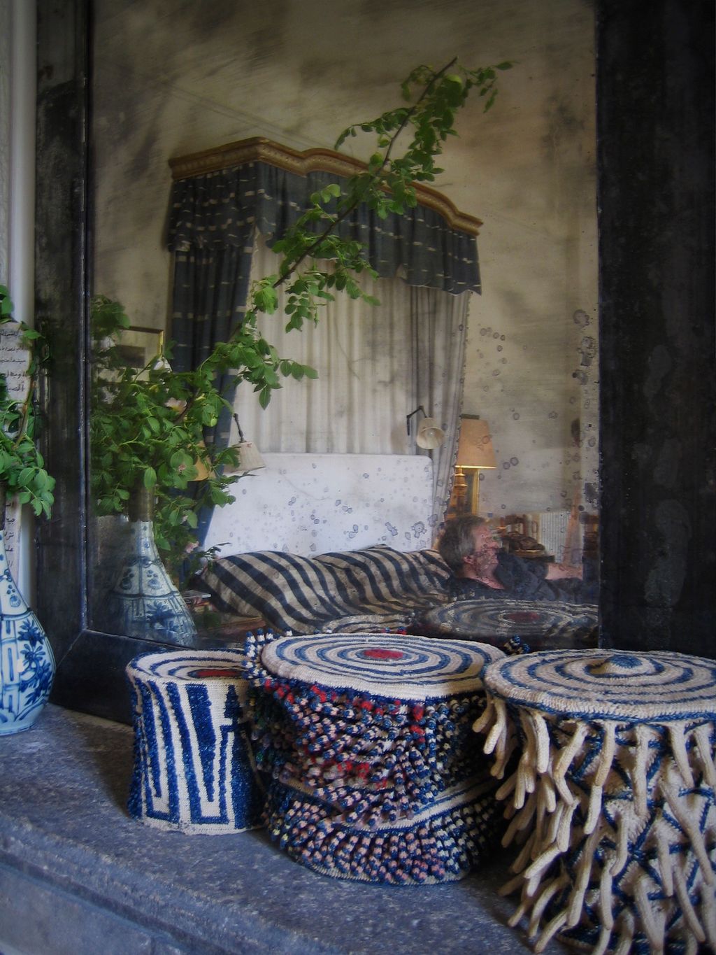A mirror reflects the halftester bed in the main bedroom. A collection of Cameroon hats stands on the mantelpiece.