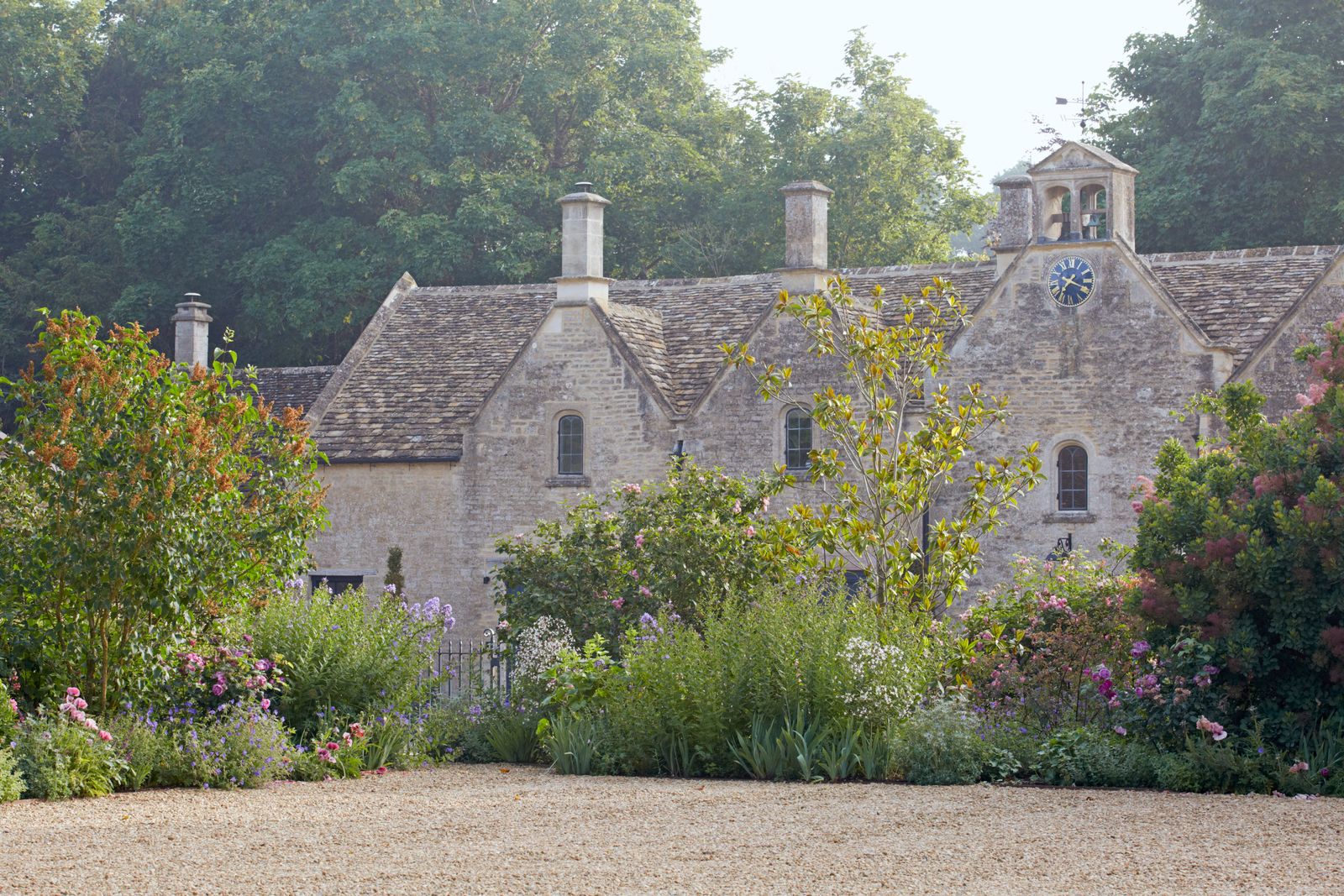 A country garden by Jinny with a backdrop of a mature trees against the Georgian stable building
