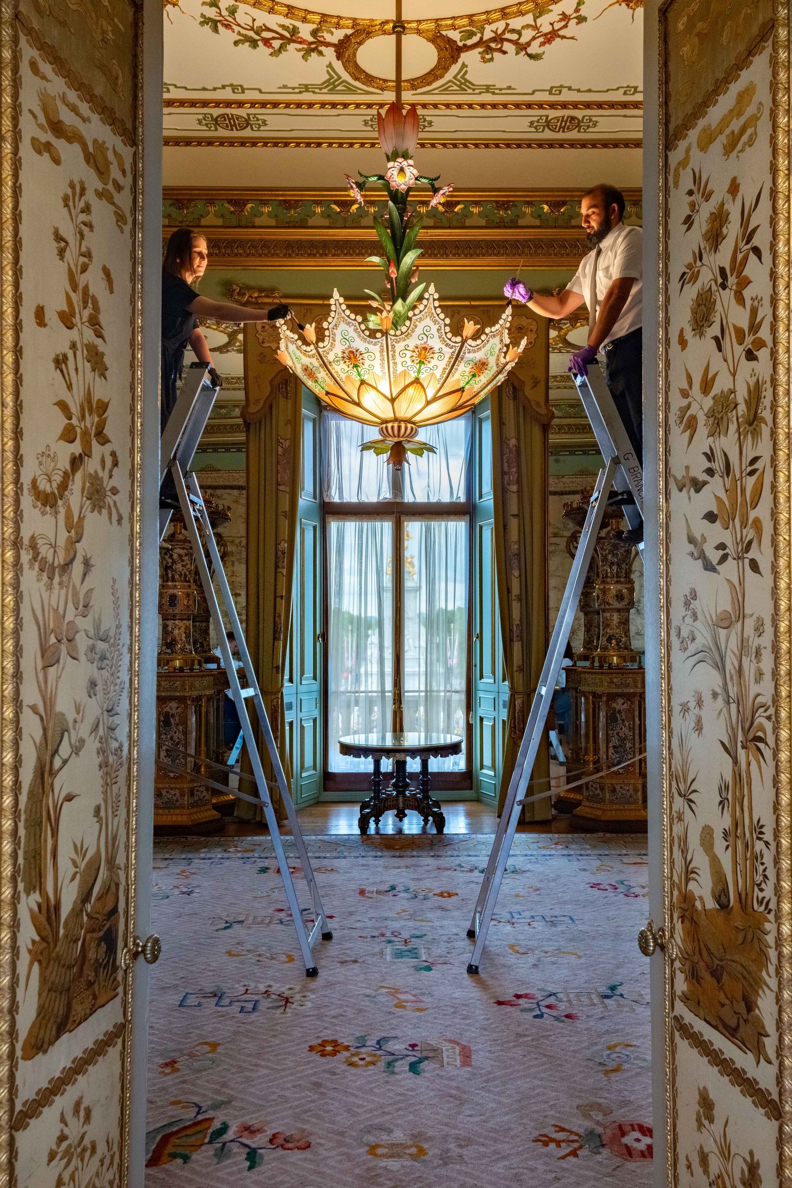 two people cleaning a chandelier in buckingham palace