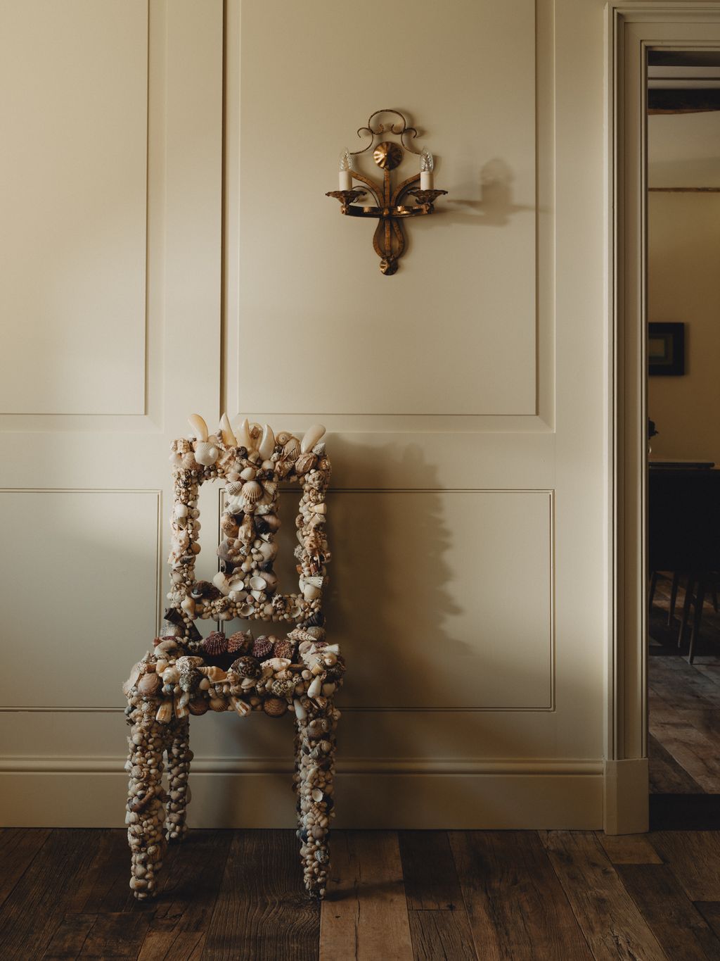A 20^th^ century shell chair from Paul De Grande Antiques stands under a 1970s Italian gilt metal wall light from Brownrigg.