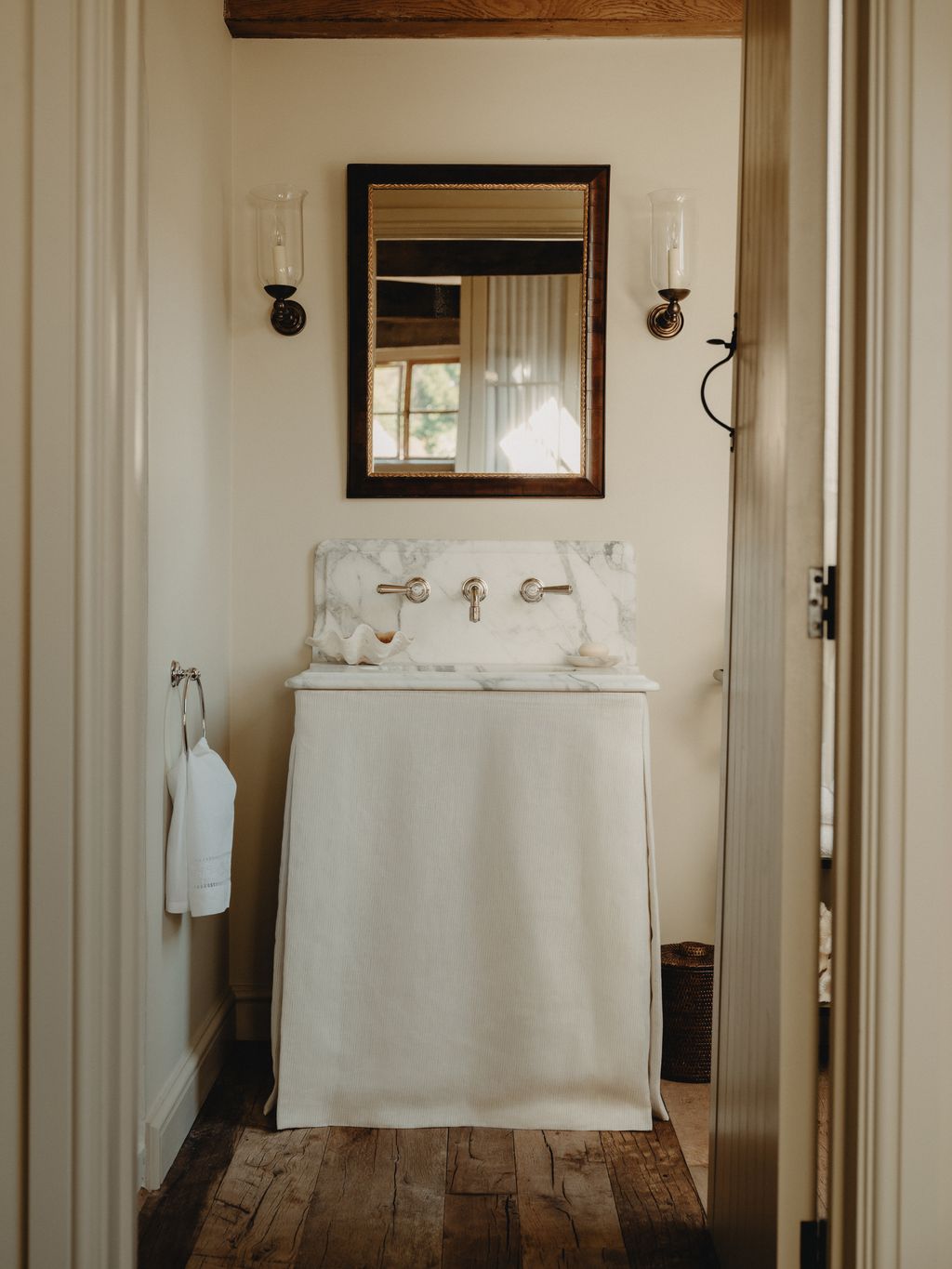 The sink has a splashback and surround in Arabescato marble and a skirt made from ‘Pampas in ivory by Threads. An...