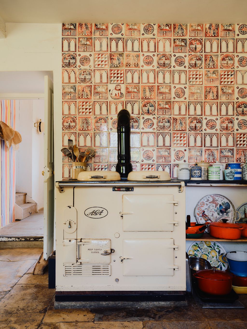 In the kitchen an old white Aga stands against colourful handpainted tiles.