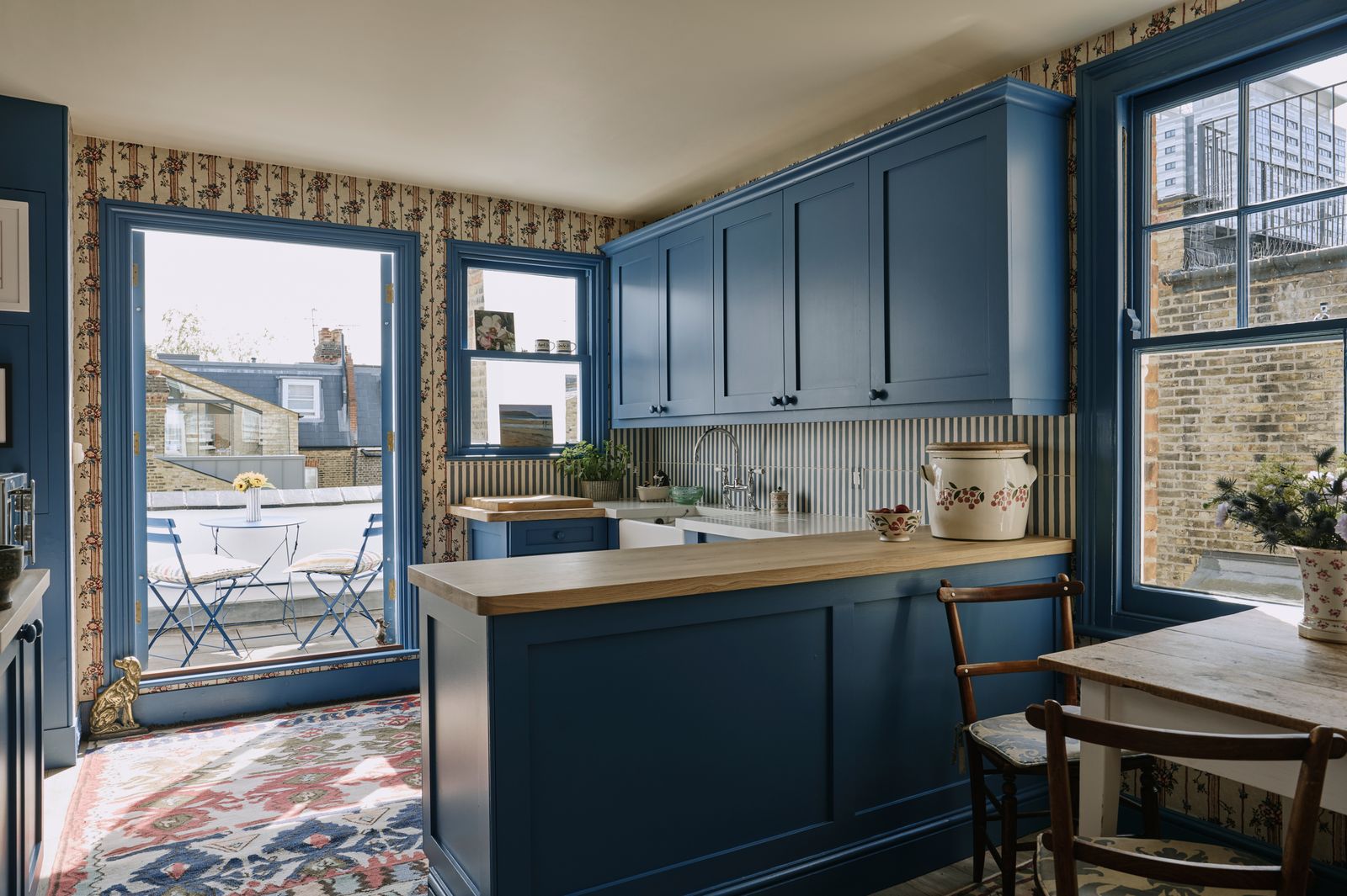 In the kitchen the floral wallpaper by Antoinette Poisson creates an eyecatching background. The cabinets are painted in...