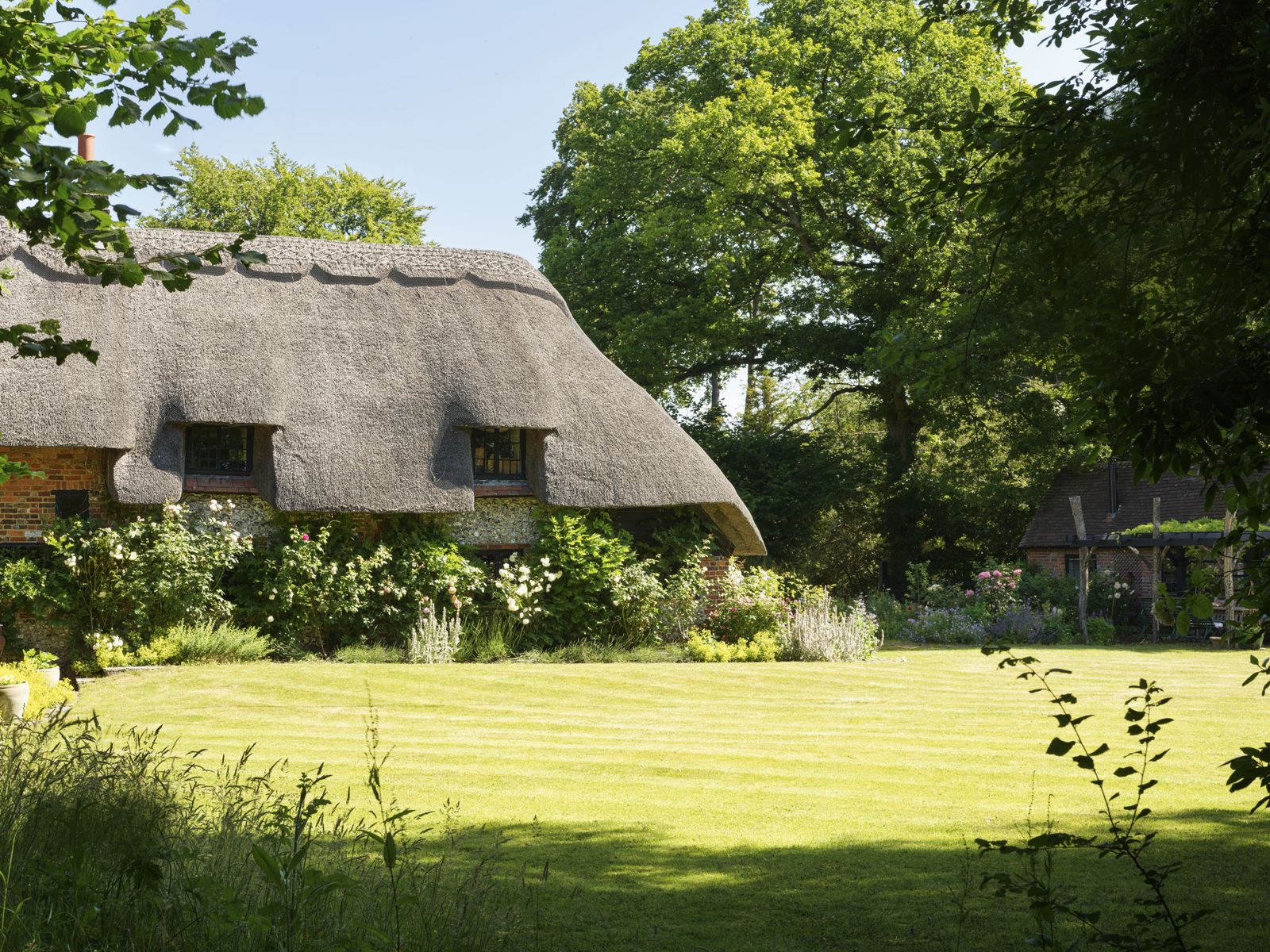 exterior of Sienna Millers country cottage with thick thatched roof draped over stone structure pictured from other side...