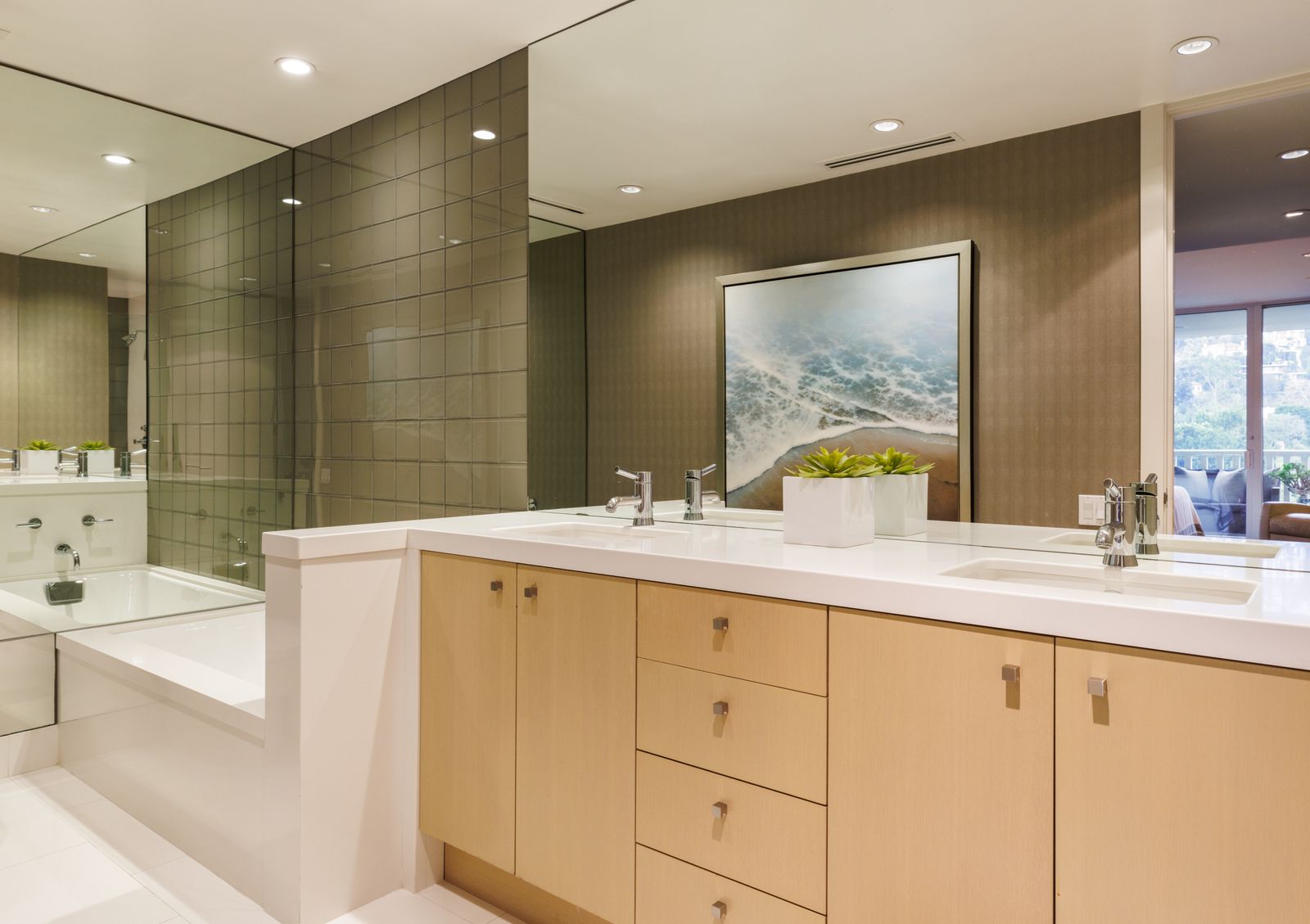 bathroom with double vanity with white countertop and blonde wood base mirrored wall tub