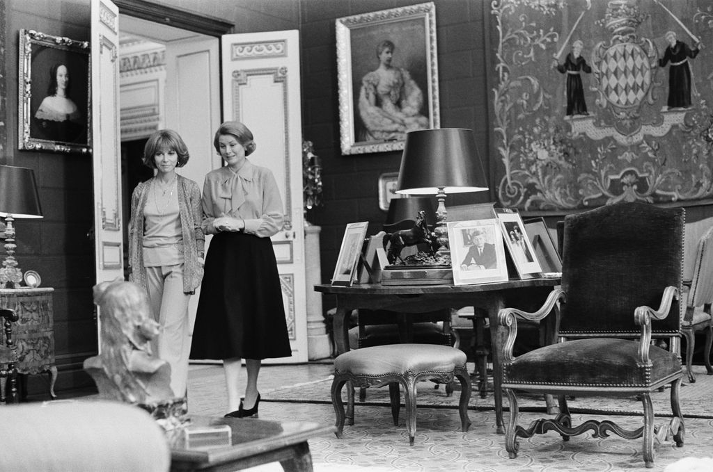 blackandwhite photo of Lee Grant left and Grace Kelly walking through an ornate room in the princes palace of Monaco